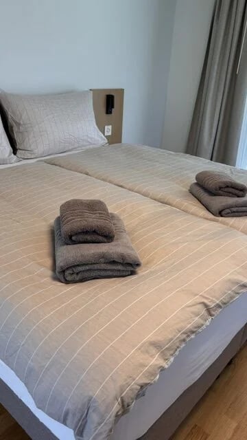 Frisch bezogenes Doppelbett mit gestreifter Bettwäsche und zwei Stapeln Frottiertücher